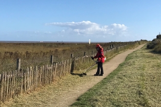 Residential volunteer strimming the pathside at Donna Nook