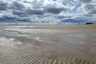 A wide beach with two people walking in the far distance