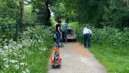 Warden and volunteers at Whisby filling in a pothole using crushed limestone and a compactor plate