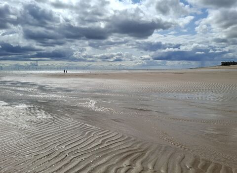 A wide beach with two people walking in the far distance